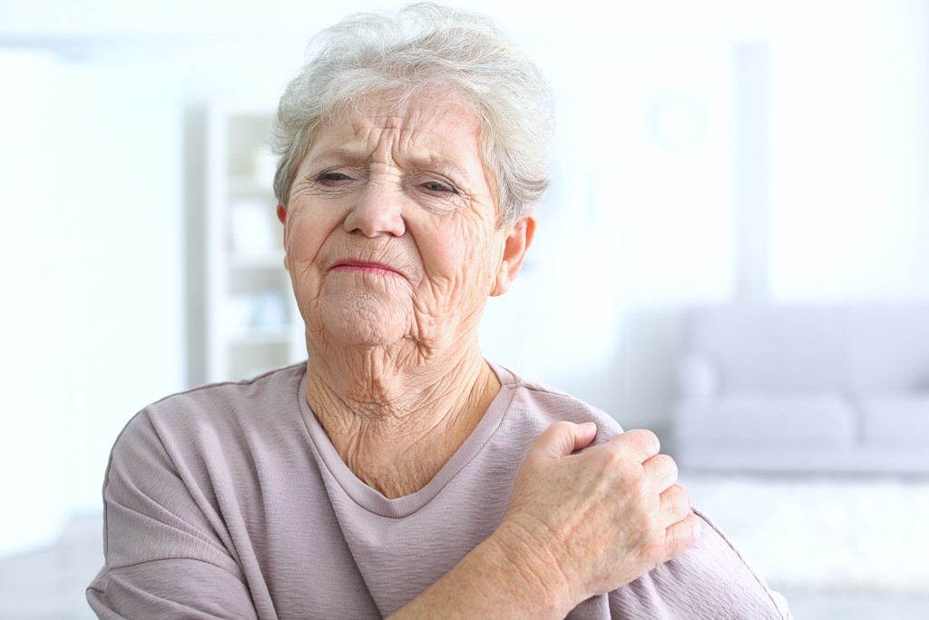 Ältere Frau hat Schmerzen in der Schulter während des Anhebens des Armes
