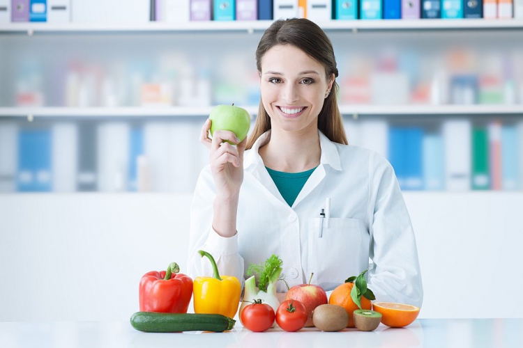 Eine Rheumatologin hält einen grünen Apfel und zeigt gesundes Gemüse und Früchte