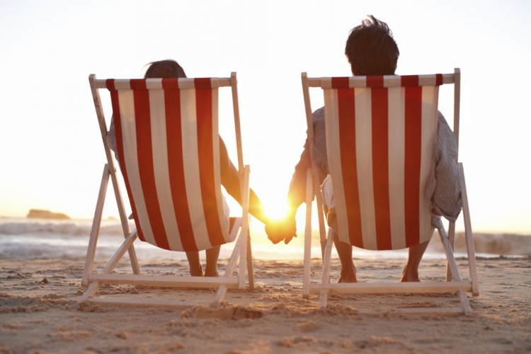In den Urlaub als Rheumatiker Ein Paar, das auf dem Strand während eines hübschen Sonnenuntergangs sitzt.